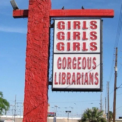 A large, red, textured sign with bold red lettering reads 'GIRLS GIRLS GIRLS' stacked above 'GORGEOUS LIBRARIANS', mounted…
