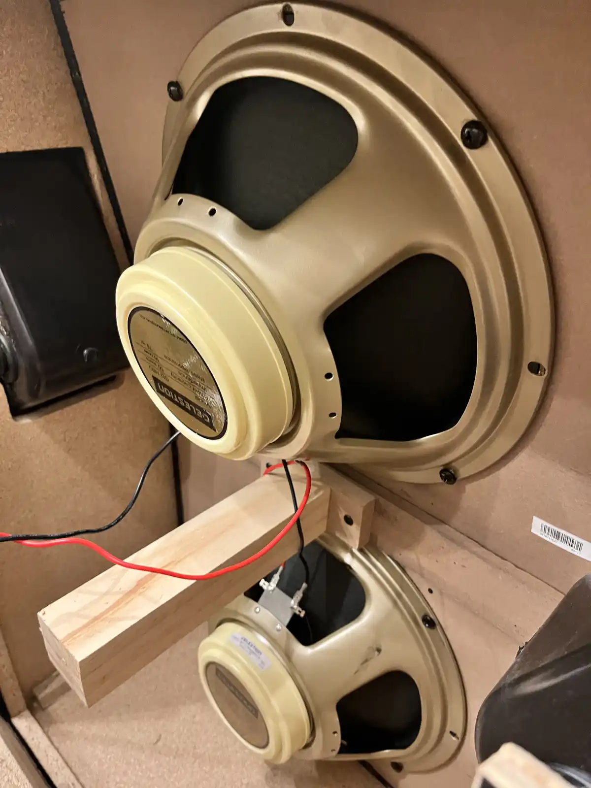 A close-up photo shows two cream-colored Celestion guitar speakers mounted inside a wooden enclosure, with one speaker…