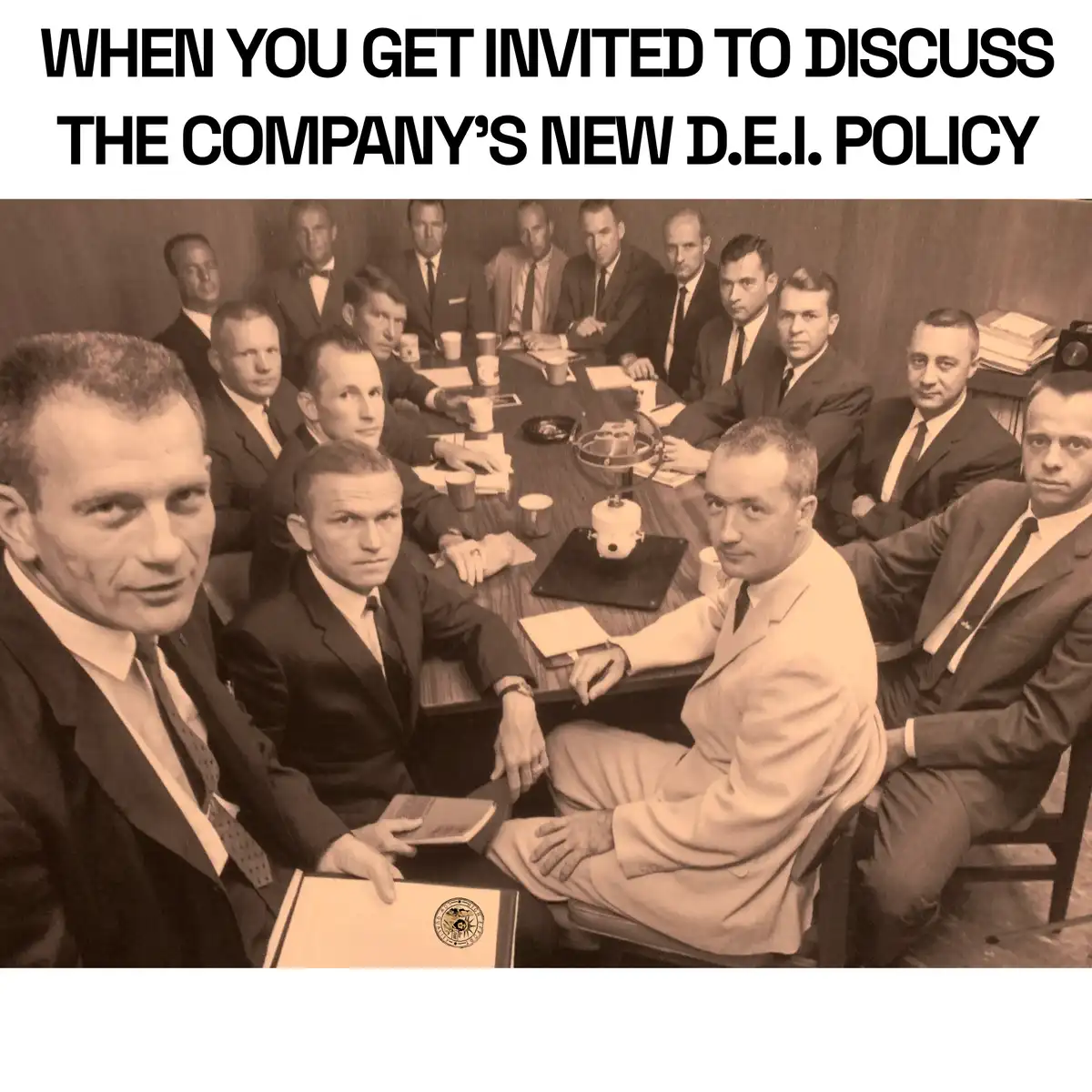 A sepia-toned historical photo shows a group of men in suits seated around a conference table, all staring intently at the…