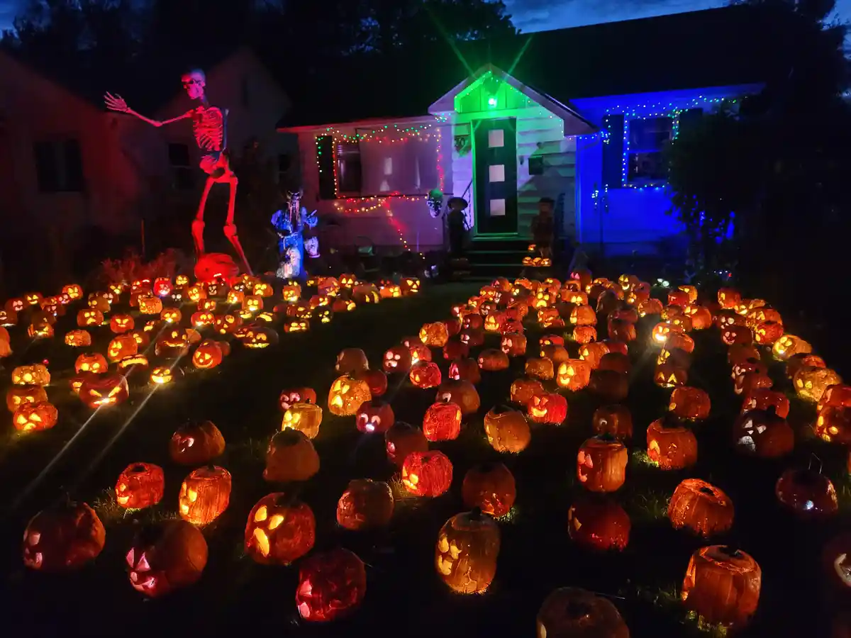 A nighttime photo of a house decorated for Halloween with hundreds of glowing jack-o'-lanterns covering the front yard, a…