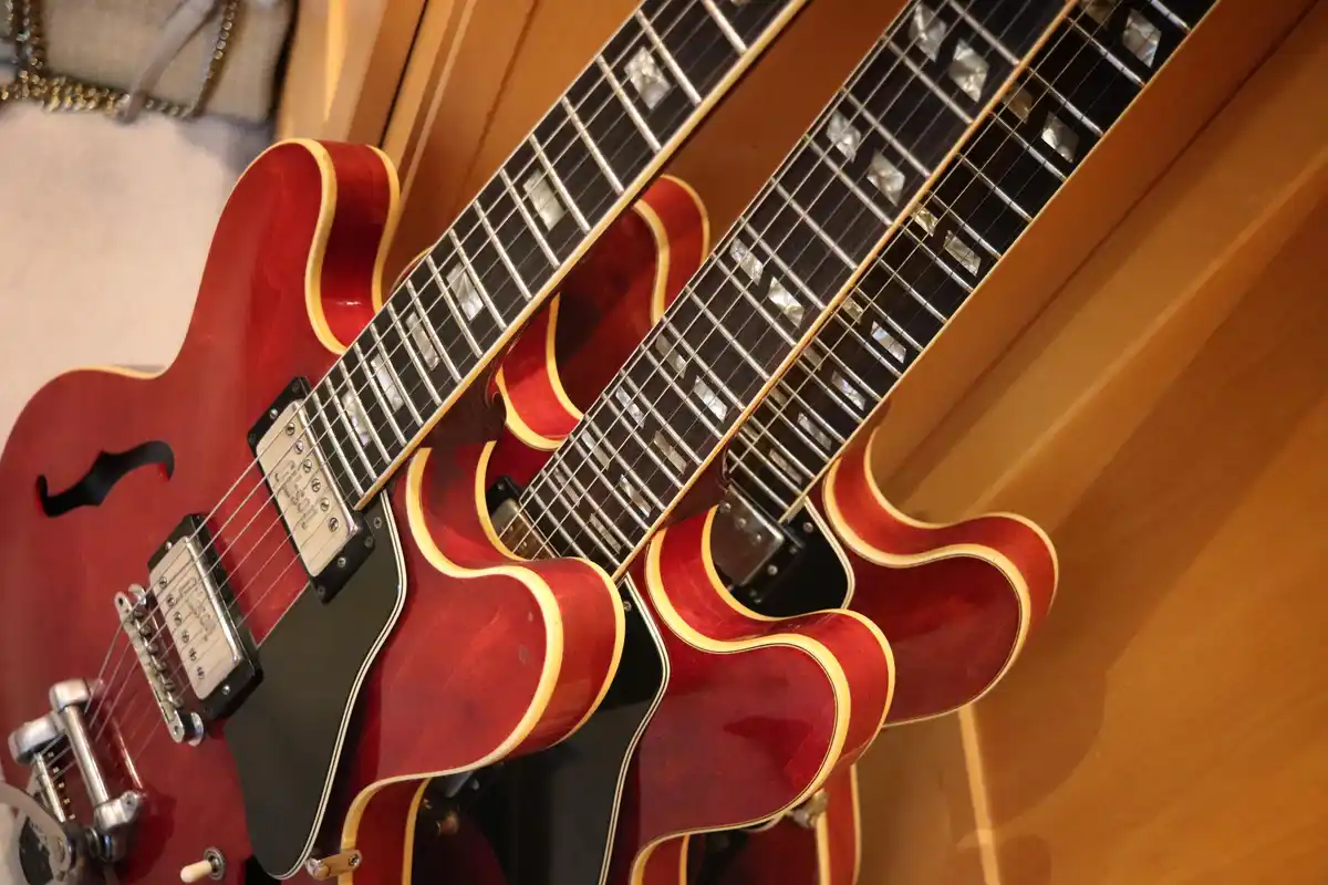 A close-up photo shows multiple identical red semi-hollow body electric guitars with black pickguards and mother-of-pearl…