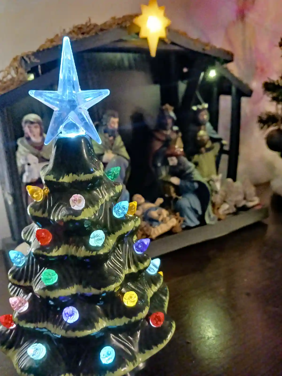 A close-up photo shows a ceramic Christmas tree ornament with multicolored lights and a glowing blue star on top, positioned…