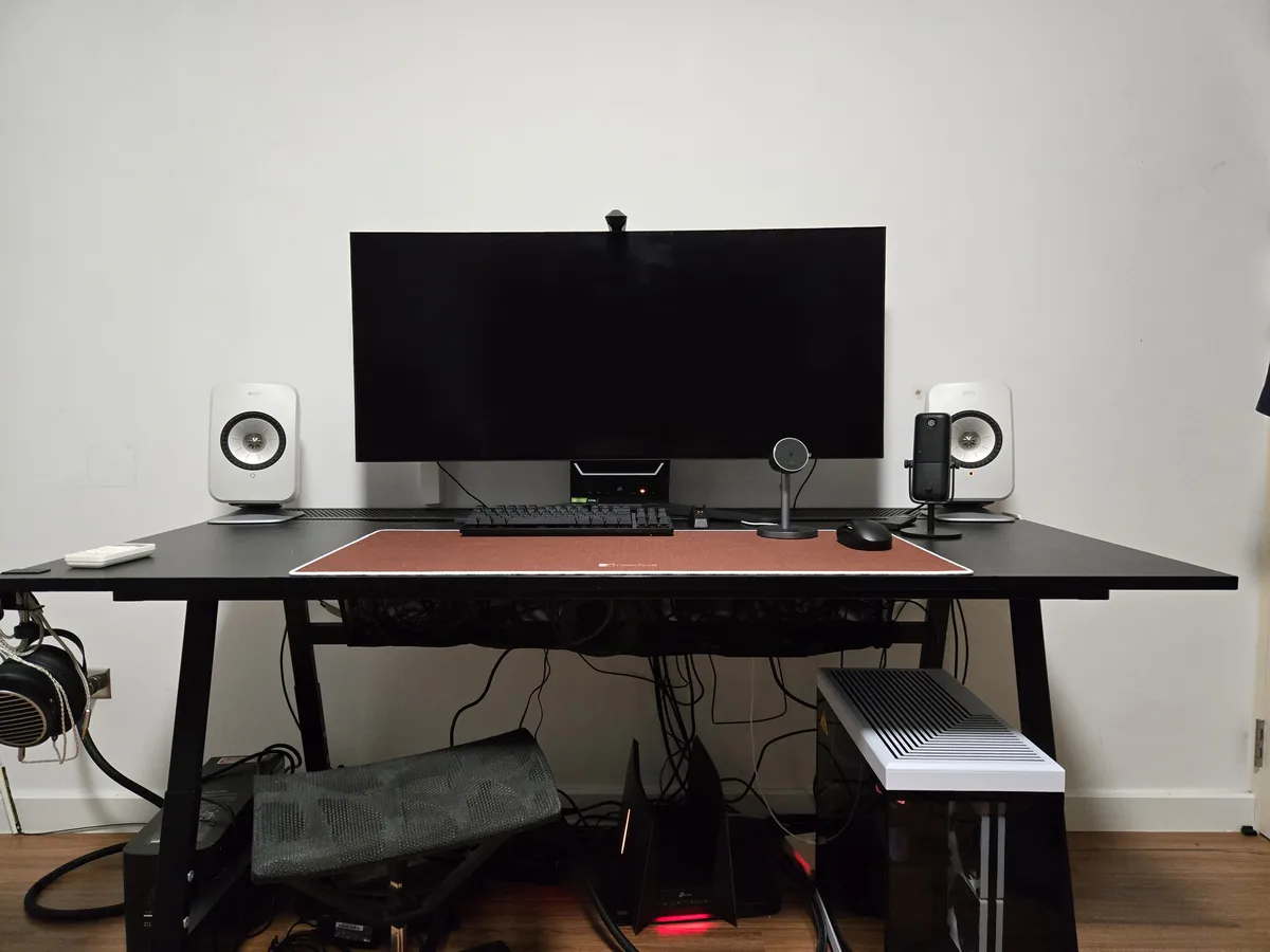A clean, modern computer desk setup with a large black monitor, white speakers, a keyboard, mouse, and microphone…
