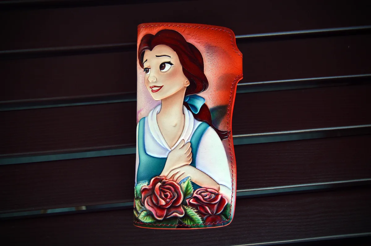 A hand-painted leather wallet features a portrait of Belle from Beauty and the Beast, wearing her iconic blue dress with a…