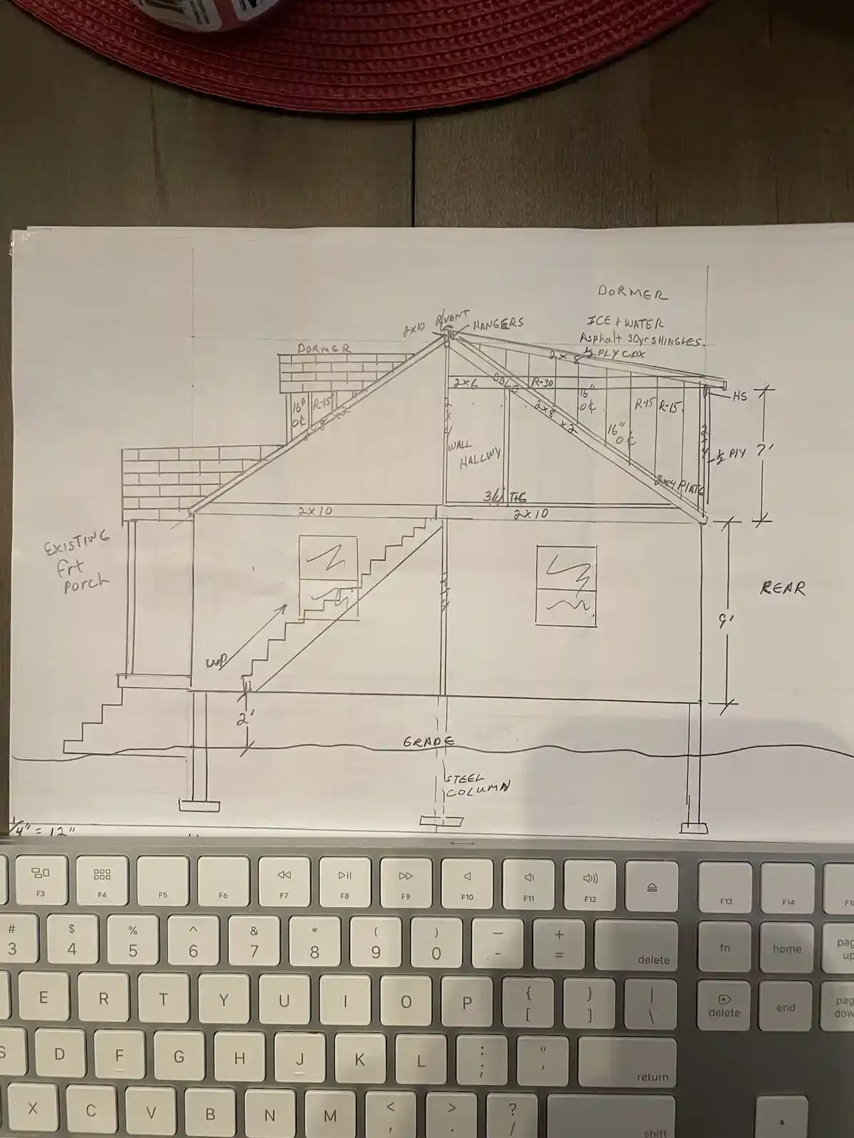 A hand-drawn architectural sketch of a house's roof and dormer structure, placed on a laptop keyboard, with detailed…
