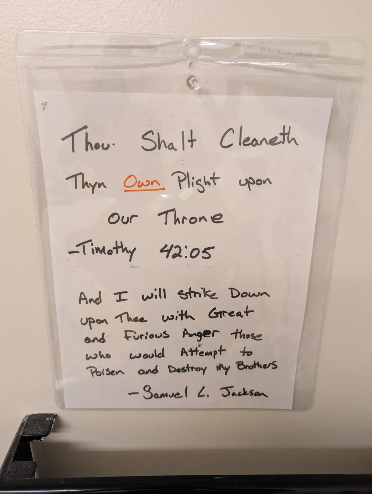 A handwritten note in a clear plastic sleeve on a wall, mimicking a religious commandment but humorously attributing it to…