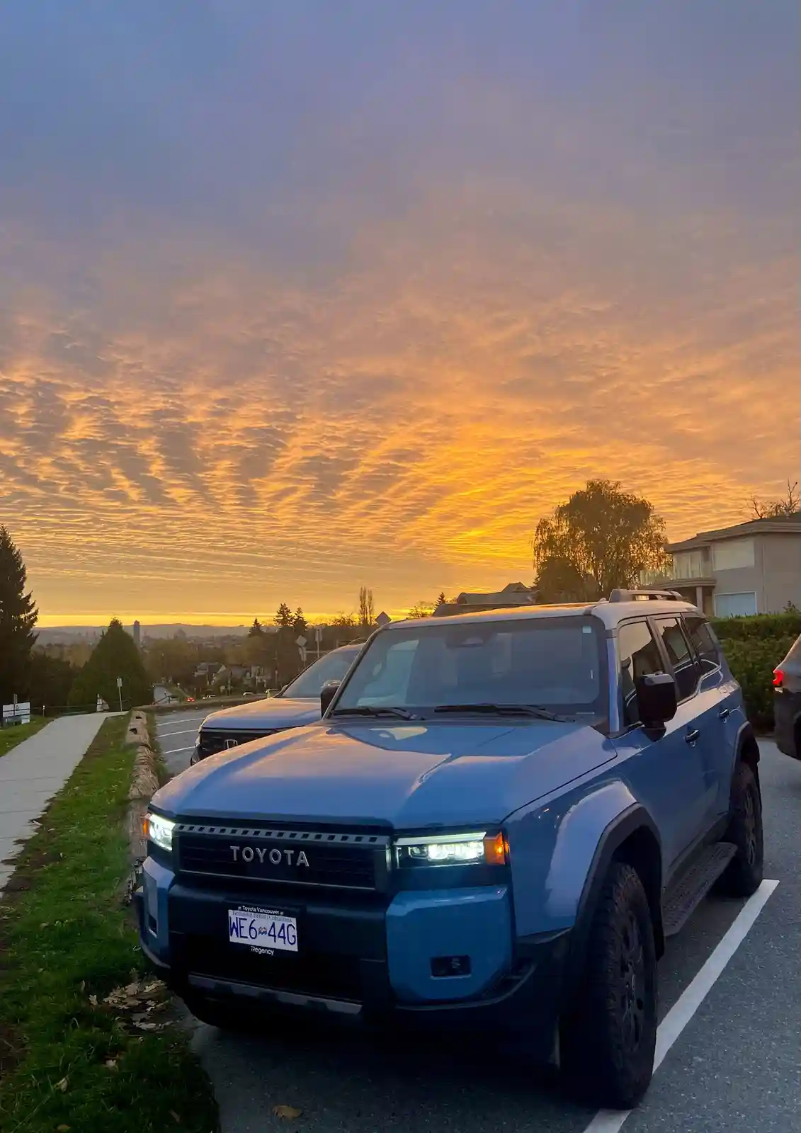 A blue Toyota bZ4X SUV is parked in a lot during a vibrant orange and purple sunset, with the overlaid text reading 'i just…