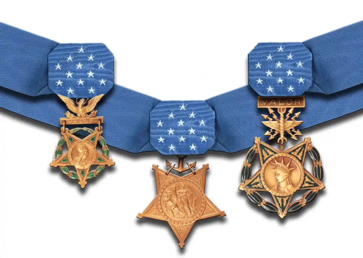 Three U.S. military valor medals — the Medal of Honor, Navy Cross, and Air Force Cross — hang on blue ribbons with white…