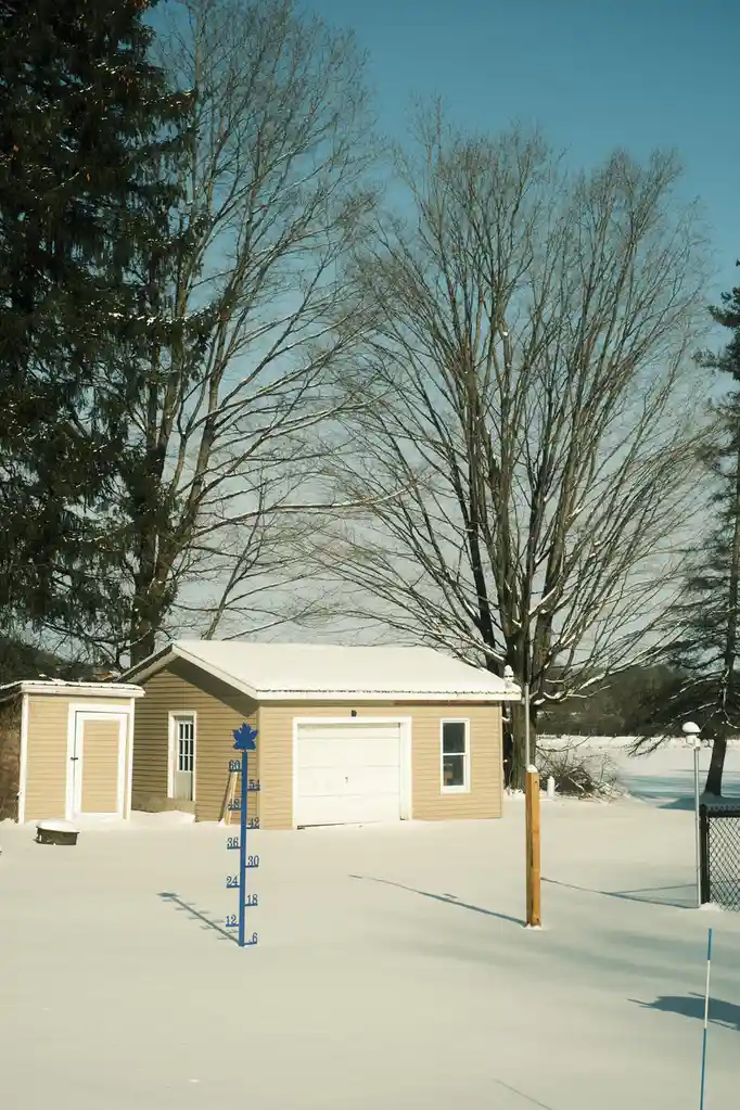 A snowy yard features a blue growth chart stick with numbers from 6 to 60 inches, topped with a maple leaf, standing in…