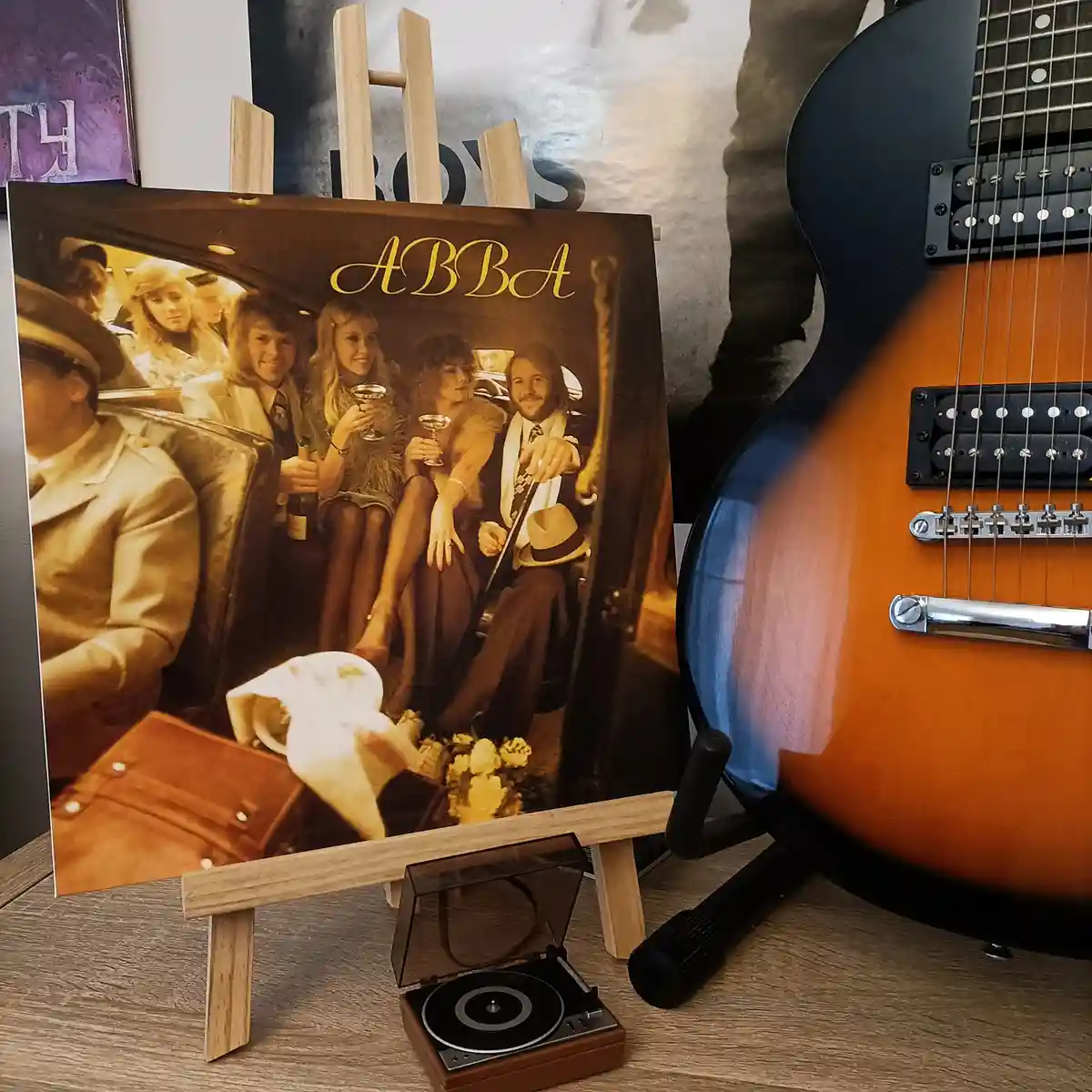 A vintage-style ABBA album cover, showing the band members in a car, is displayed on a small wooden easel. Beside it, a…