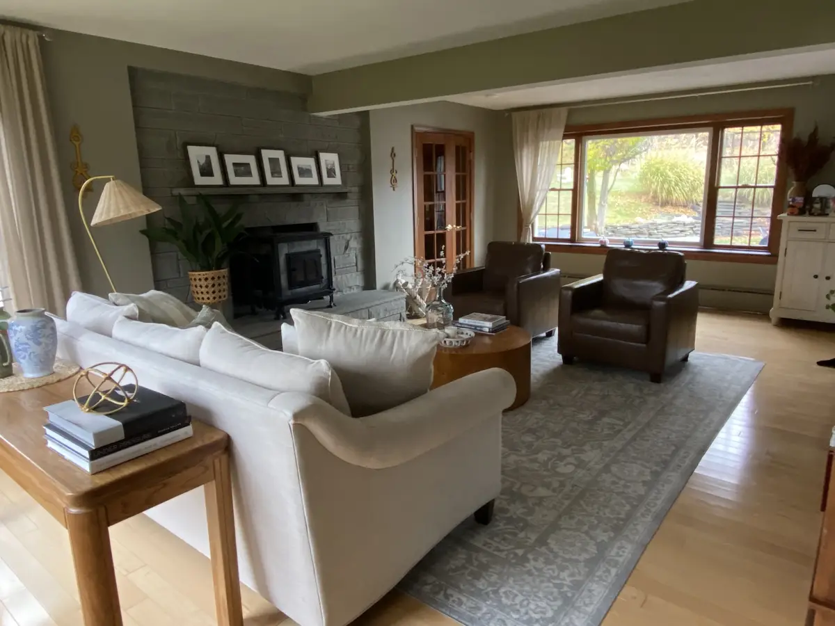 A well-lit, spacious living room with a beige sofa, two brown leather armchairs, a wooden coffee table, and a stone…