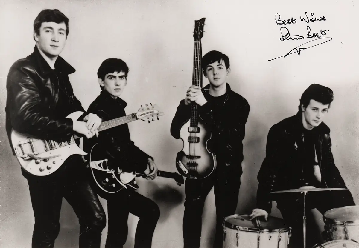 A black-and-white photo of The Beatles in their early days, holding guitars and drums, with a handwritten note in the top…