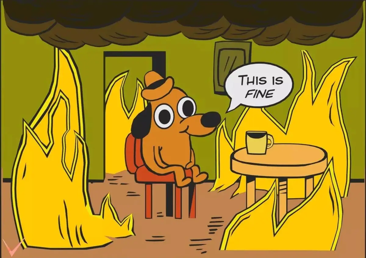 A cartoon dog wearing a hat sits calmly in a room engulfed in flames and smoke, smiling while saying 'THIS IS FINE' in a…