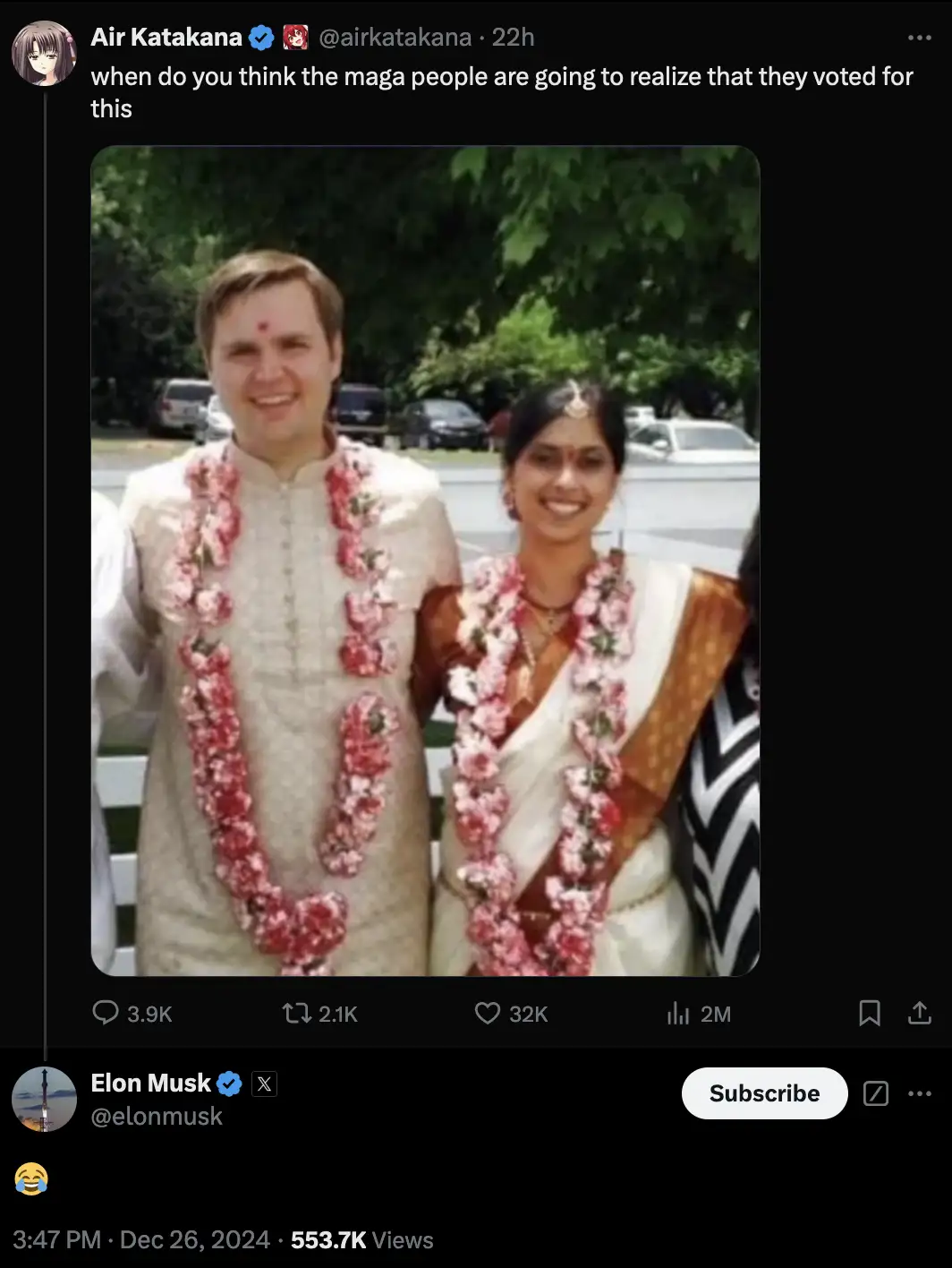 A photo shows a smiling man and woman dressed in traditional Indian wedding attire, both wearing floral garlands and bindis…