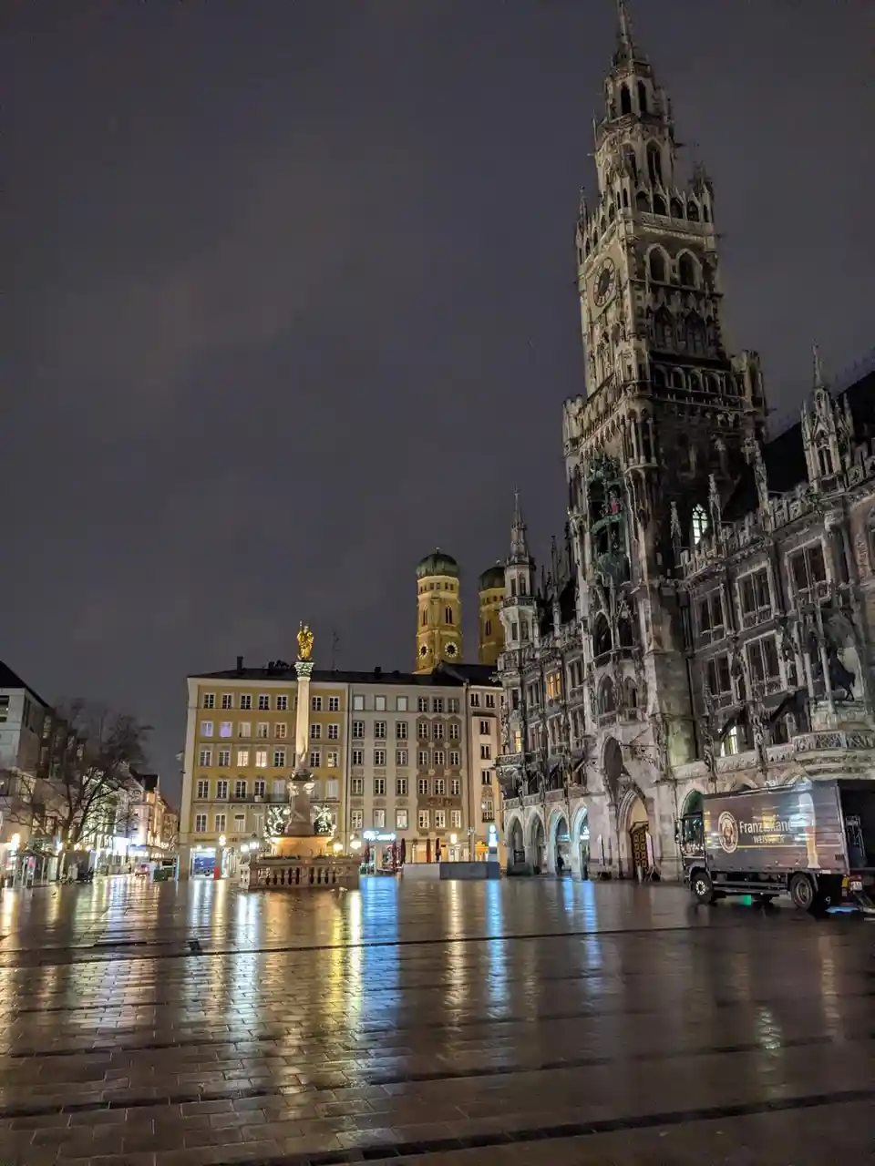 A nighttime photo of Marienplatz in Munich, Germany, showing the illuminated New Town Hall with its tall Gothic tower, the…
