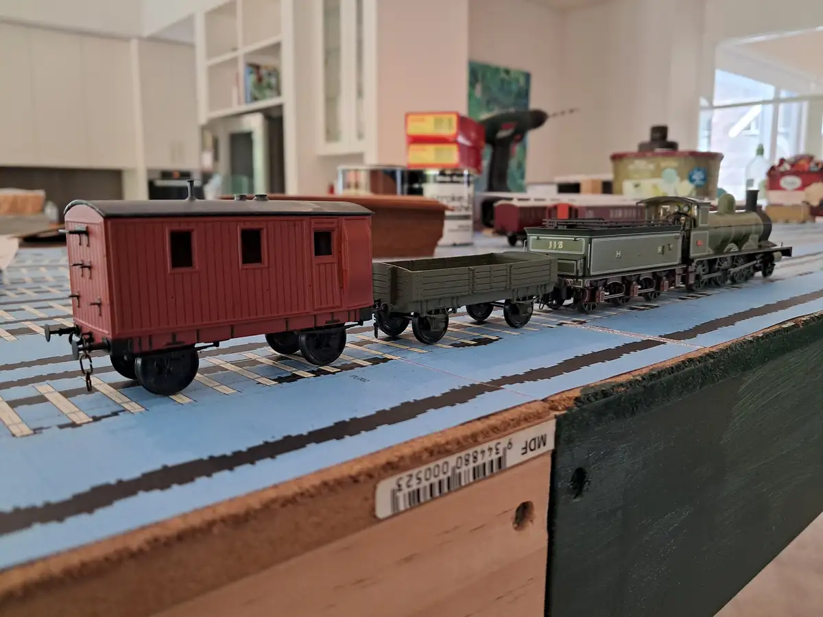 A close-up photo of a model train set on a blue track with a red caboose and green locomotive. The background shows a…