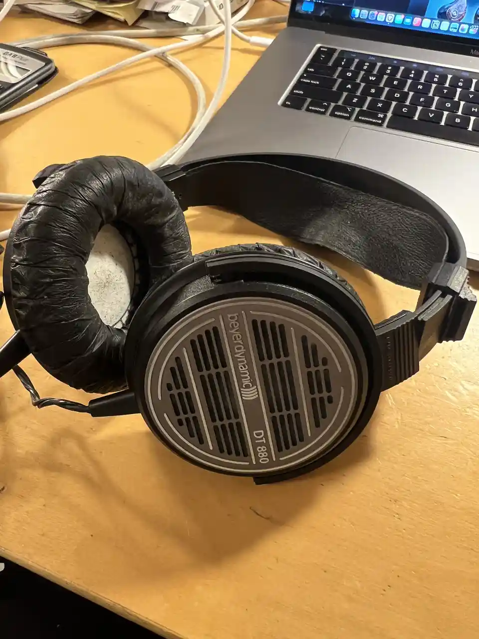 A pair of black Beyerdynamic DT 880 over-ear headphones sits on a wooden desk, with one earcup covered in crumpled black…