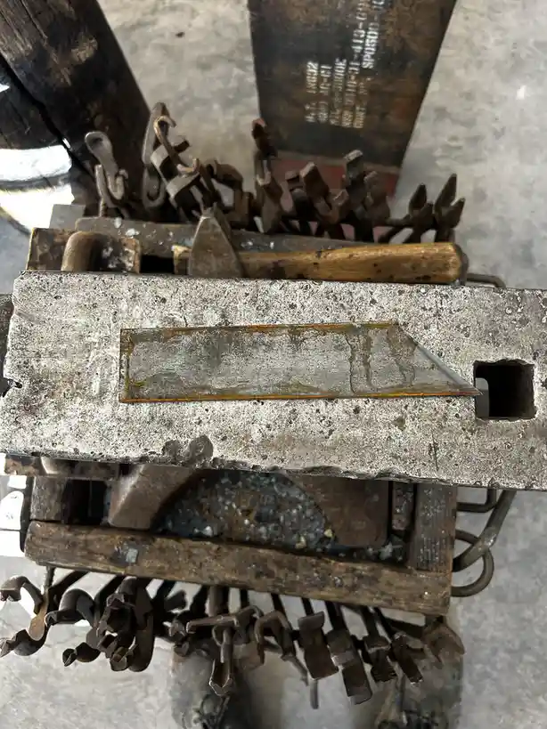 A close-up photo of a heavily used, rusty metal workbench or tool rack filled with various worn-out metal tools like hooks…