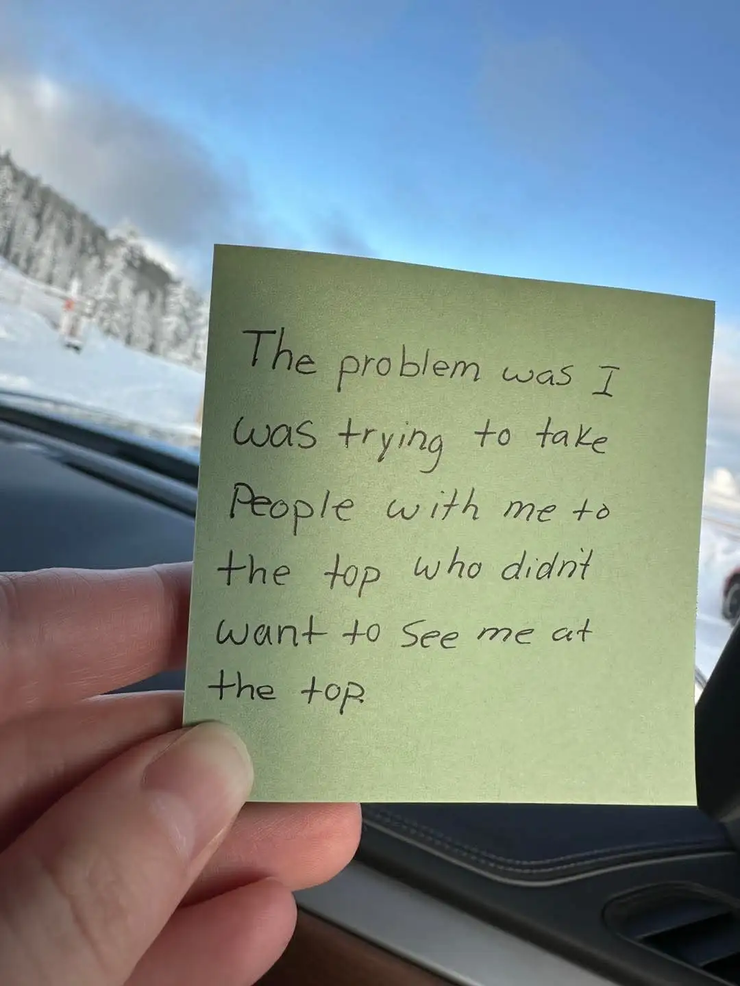 A hand holds a green sticky note inside a car, with handwritten text that reads 'The problem was I was trying to take people…