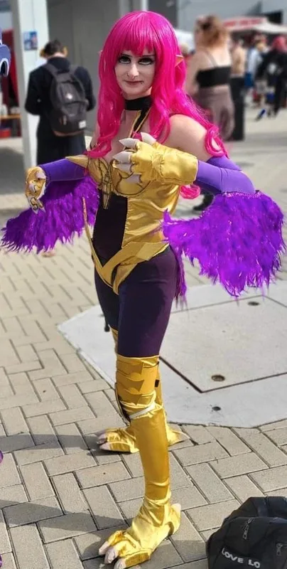 A person in a detailed cosplay of a character with bright pink hair, pointed ears, and a gold and purple outfit with…
