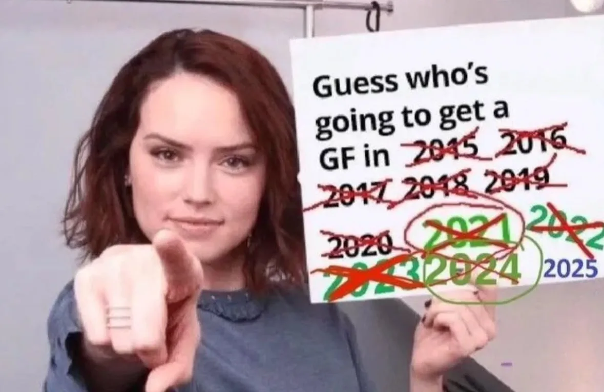 A woman with brown hair and a ring on her finger points directly at the viewer while holding a white sign. The sign reads…