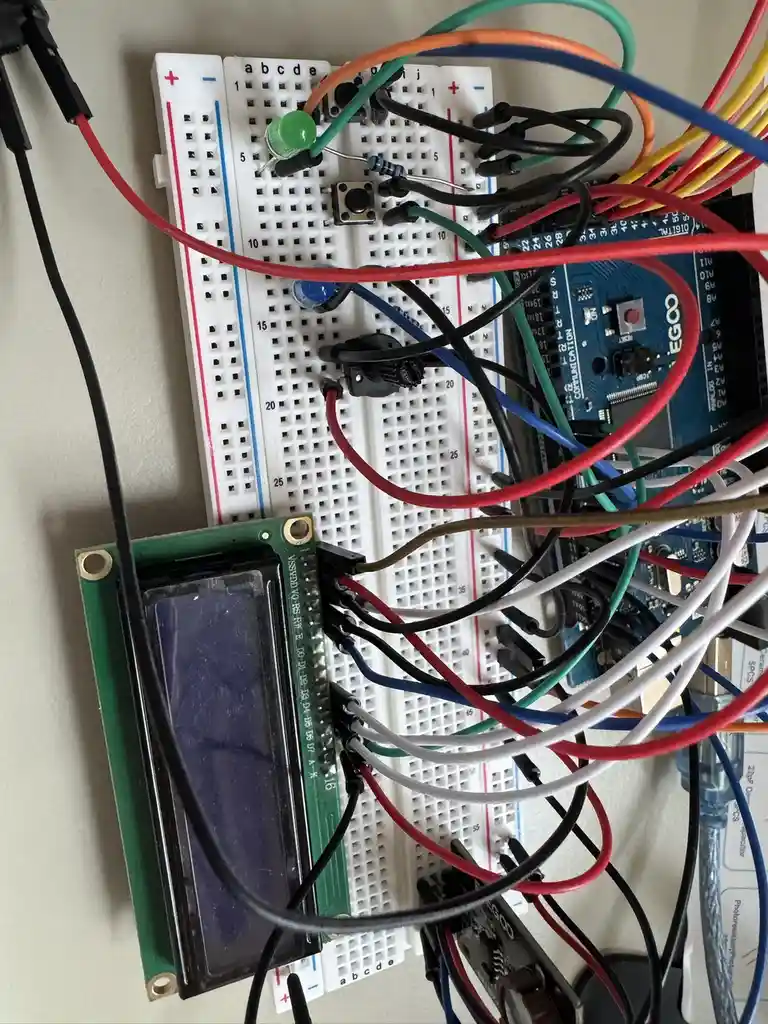 A messy electronics project on a white breadboard with tangled multicolored wires connecting various components including an…