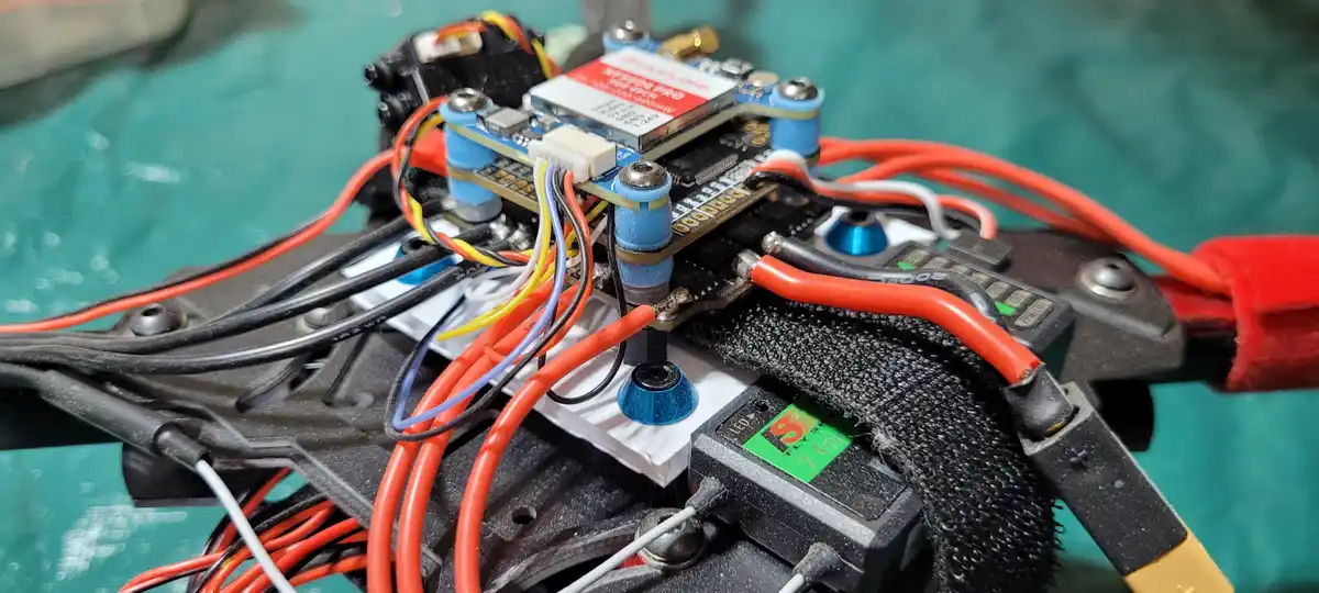 A close-up photo of a densely wired drone's internal electronics, showing a circuit board, various connectors, red and black…