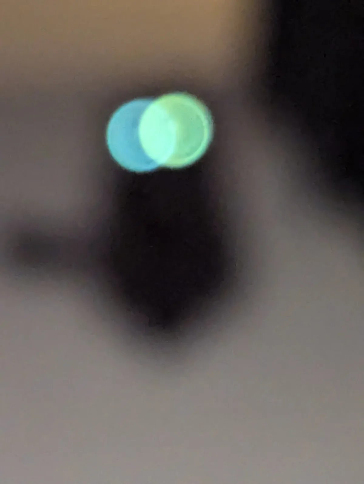 A blurry, low-resolution photo shows two overlapping glowing circles, one cyan and one lime green, resembling eyes…