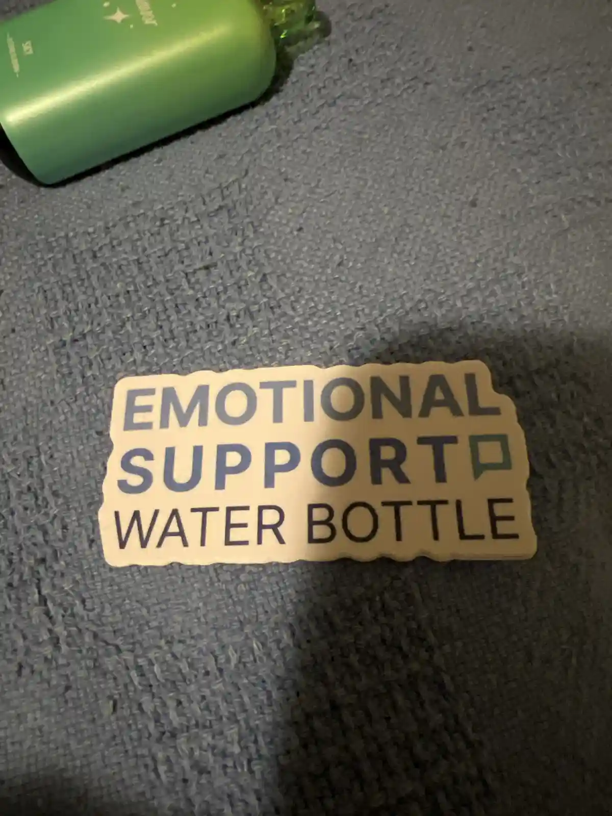 A close-up photo shows a beige sticker with the text 'EMOTIONAL SUPPORT WATER BOTTLE' in bold, sans-serif font, placed on a…