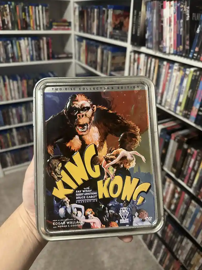 A hand holds a metal tin DVD case for the 1933 classic 'King Kong,' featuring the iconic artwork of the giant ape carrying a…