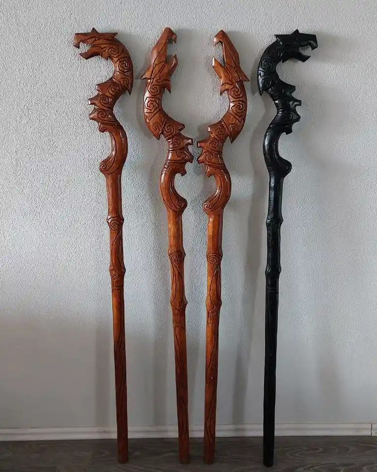 Four intricately carved wooden staffs with dragon heads are standing upright against a plain wall. Three are light brown…