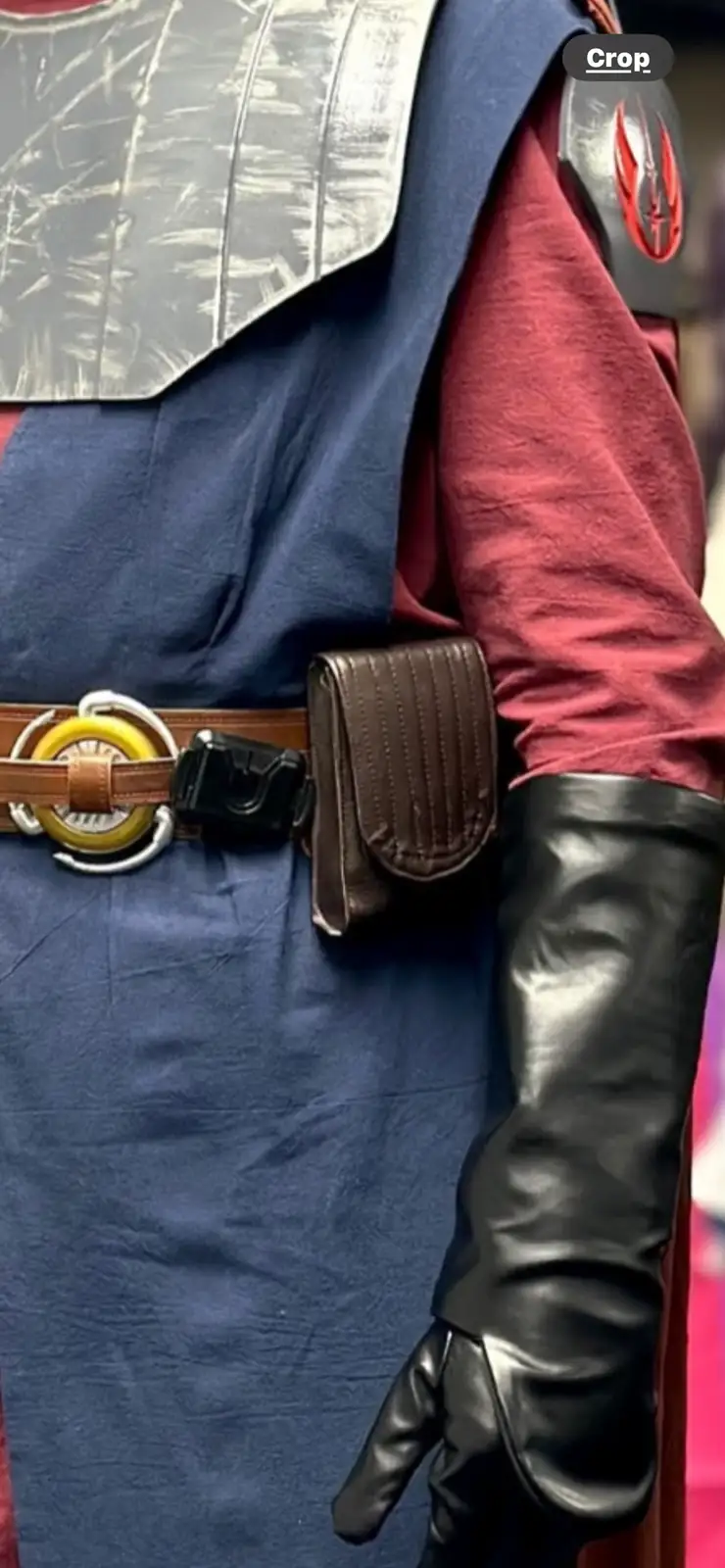 A close-up of a person in a Star Wars costume, showing a blue tunic, red shirt, silver armor, and a belt with a yellow…