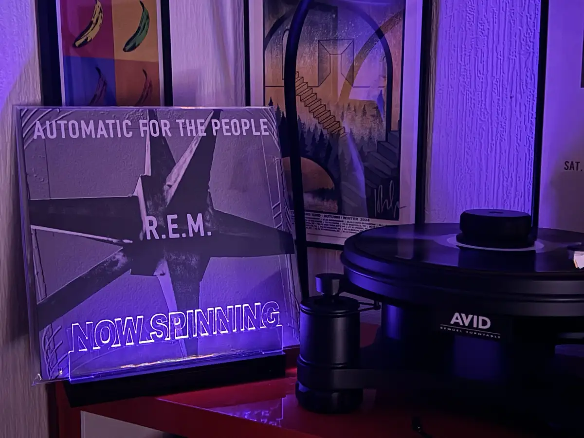 A vinyl record player sits next to a glowing acrylic display of the R.E.M. album 'Automatic for the People', which has the…