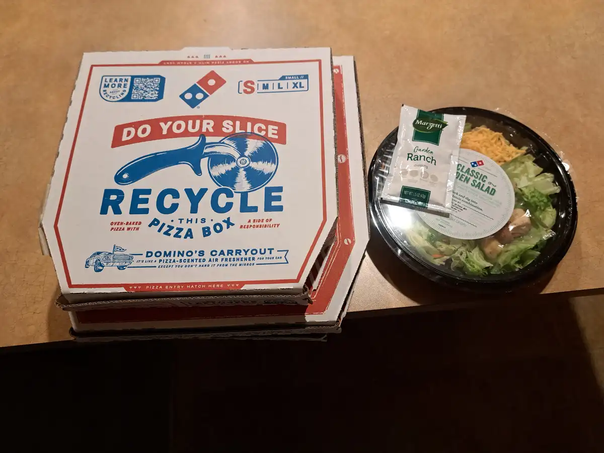 A Domino's pizza box with the slogan 'DO YOUR SLICE RECYCLE THIS PIZZA BOX' is shown next to a classic garden salad with…