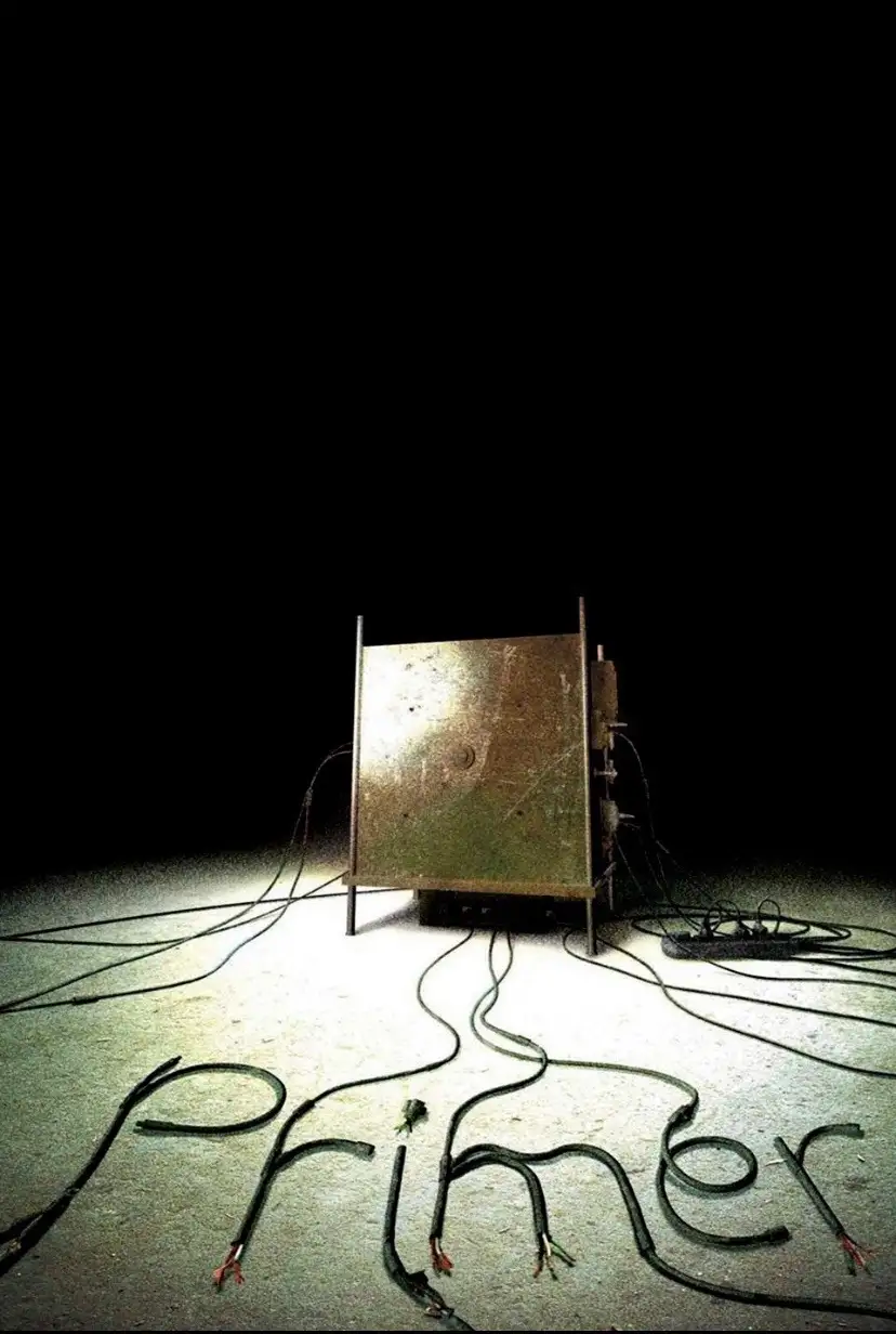 A dark, minimalist image shows a rusty metal box on a concrete floor, surrounded by tangled black electrical wires. The…