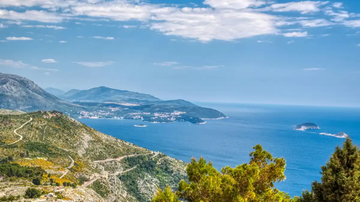 Turquoise Adriatic Sea sparkles beneath a brilliant blue sky, as the ancient city of Dubrovnik's stone walls and red-tiled…