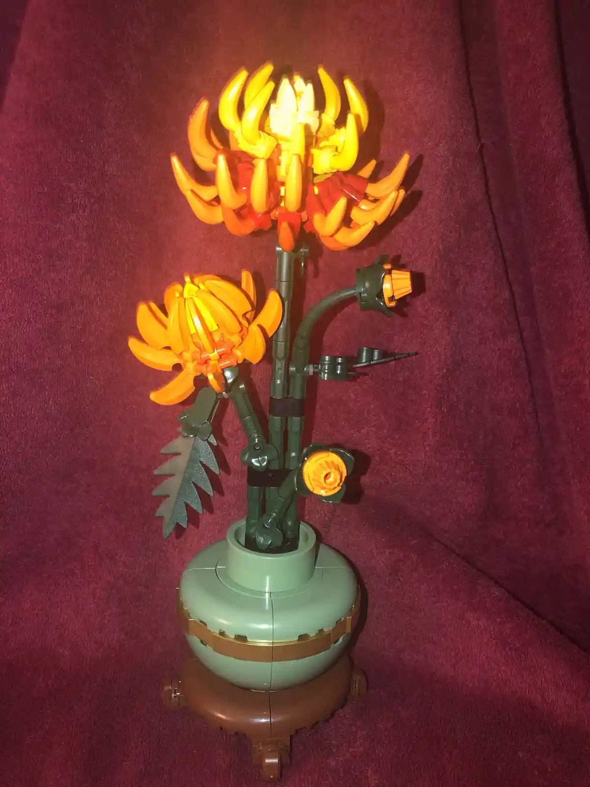 A LEGO model of a plant with multiple orange and yellow flower heads, some resembling flames or spikes, set in a green pot…