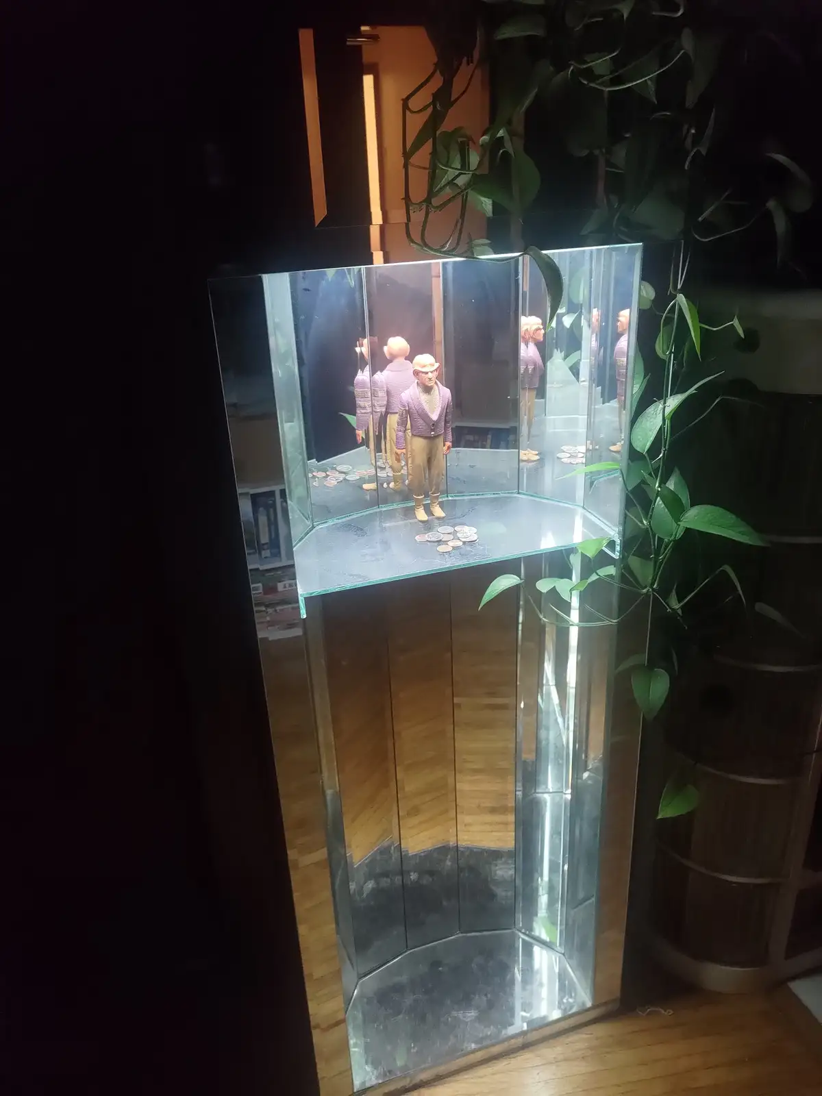 A small figurine of a man in a purple sweater and beige pants stands inside a glass display case, surrounded by multiple…