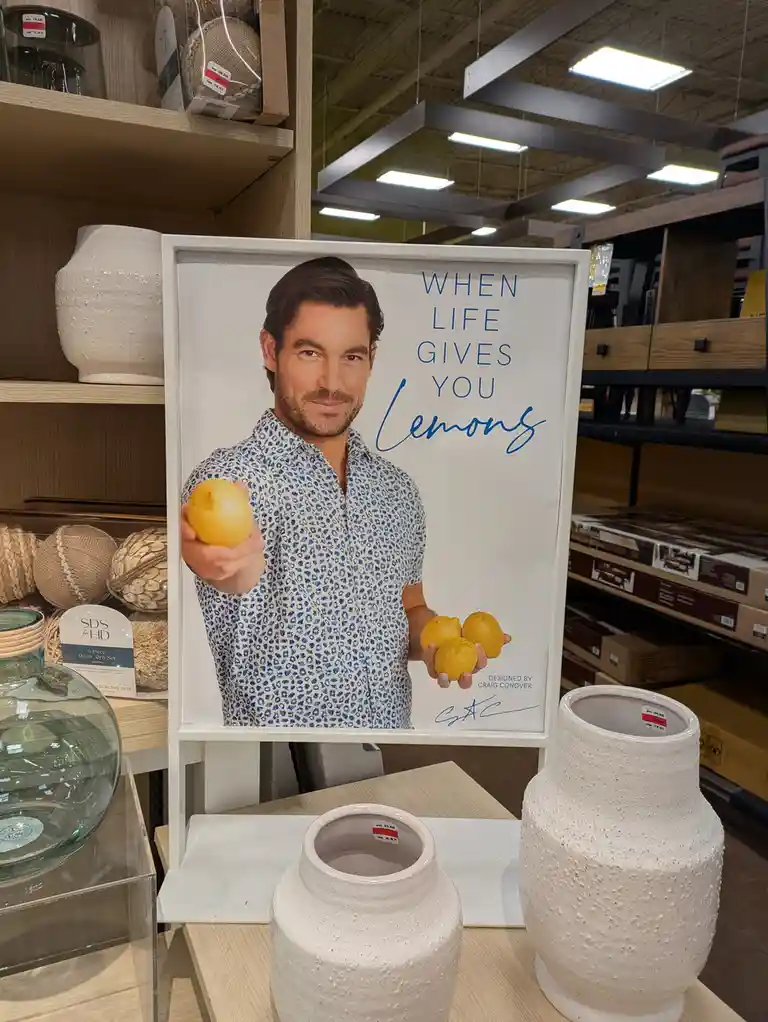 A framed decorative poster in a home goods store shows a man holding lemons with the text 'WHEN LIFE GIVES YOU Lemons' next…