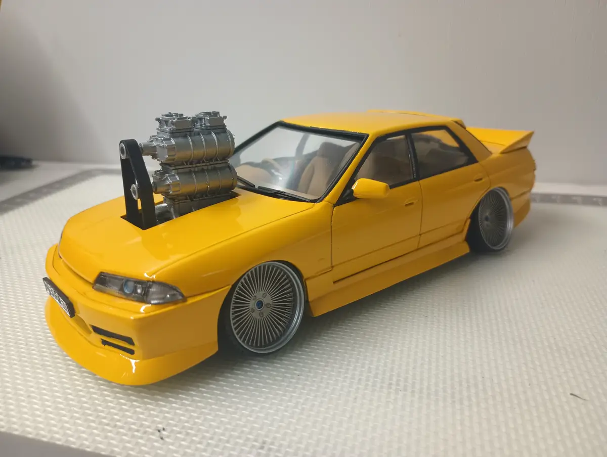 a yellow die-cast model car, resembling a BMW E30, is shown with a large, silver supercharged engine mounted on top of its…
