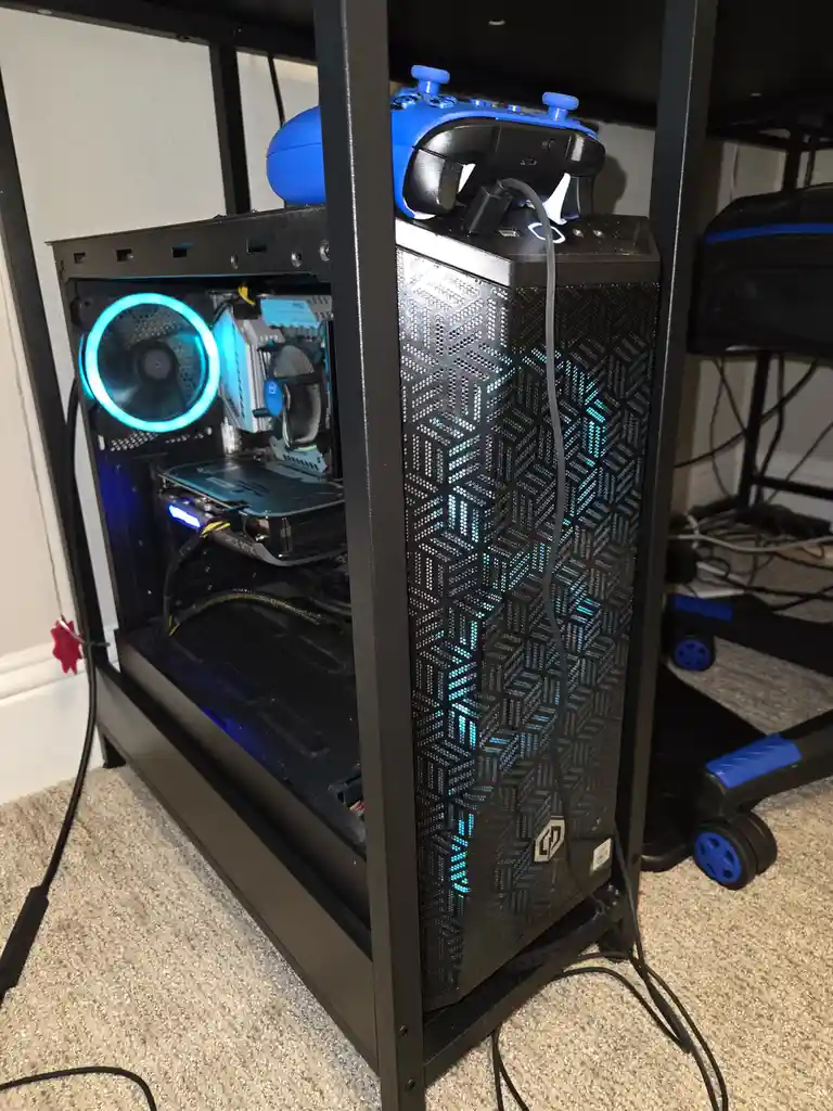 A black computer case with blue internal lighting and a visible GeForce RTX graphics card sits on a stand, with a blue Xbox…