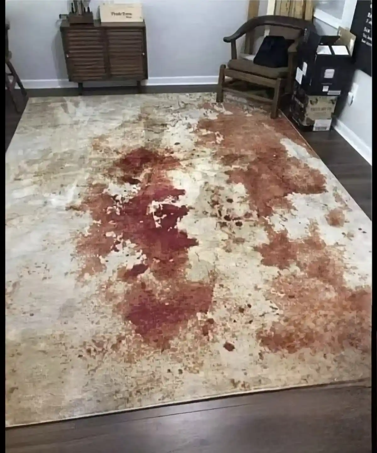 A large, beige and brown patterned rug with faded, abstract red and brown splotches that resemble a map of the world, laid…