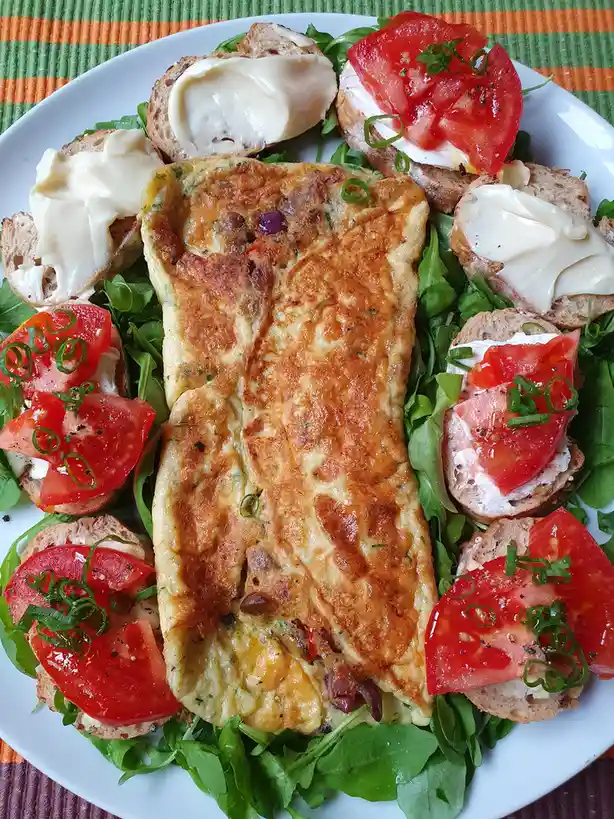 A plate of food features a golden-brown omelet shaped like a human torso, surrounded by small bread slices topped with…
