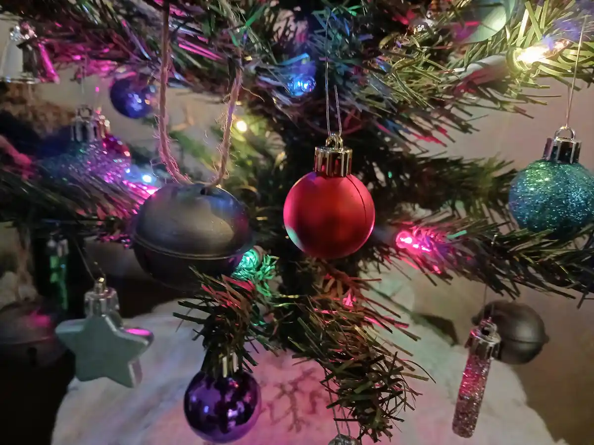 A close-up photo of a decorated artificial Christmas tree with colorful ornaments, including a red ball, glittery blue and…