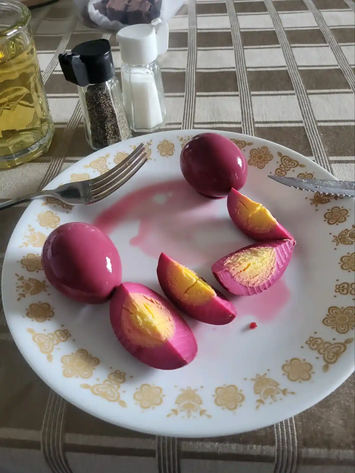 A plate of hard-boiled eggs dyed a vibrant purple, with some cut open to reveal yellow yolks, sits on a patterned tablecloth…