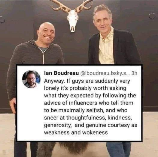 Two men stand smiling in front of a mounted deer skull. A tweet from Ian Boudreau is overlaid on the image, criticizing…