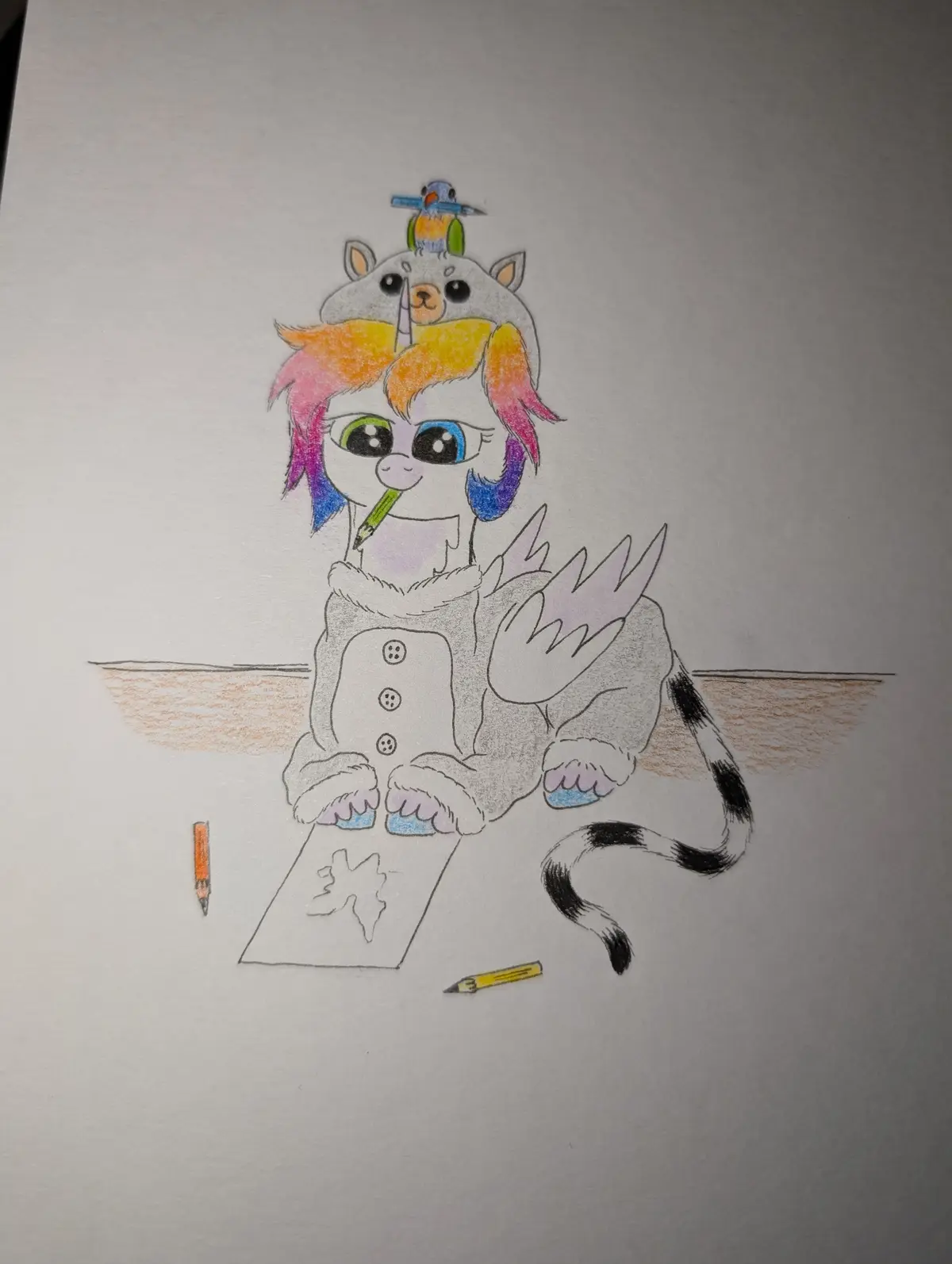 A colorful cartoon drawing shows a winged, horned creature with rainbow hair and a cat-like headpiece, sitting at a desk…