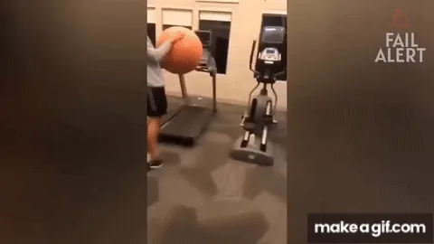 A man in a gym is seen attempting to walk on a treadmill while carrying a large orange basketball. He struggles to maintain…