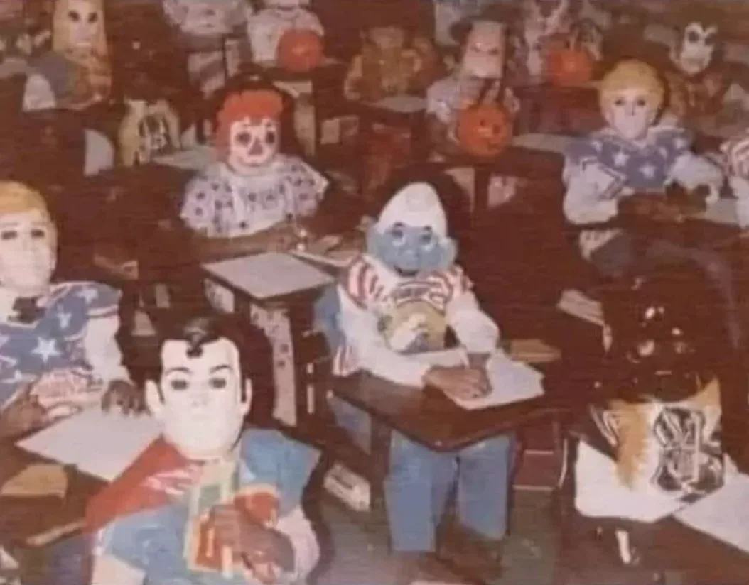 A grainy, vintage classroom photo shows numerous children wearing full-body costumes of various cartoon and movie…