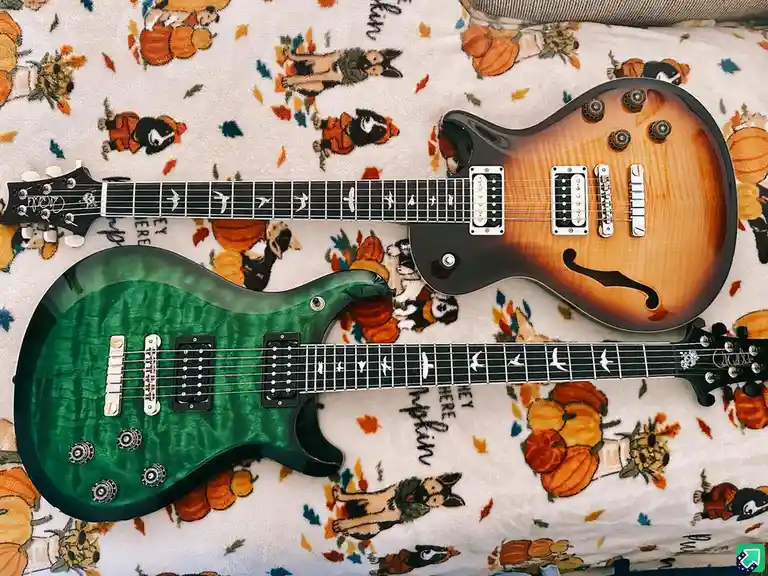 Two electric guitars, one green and one sunburst, lie on a white blanket with a repeating pattern of cartoon dogs in…